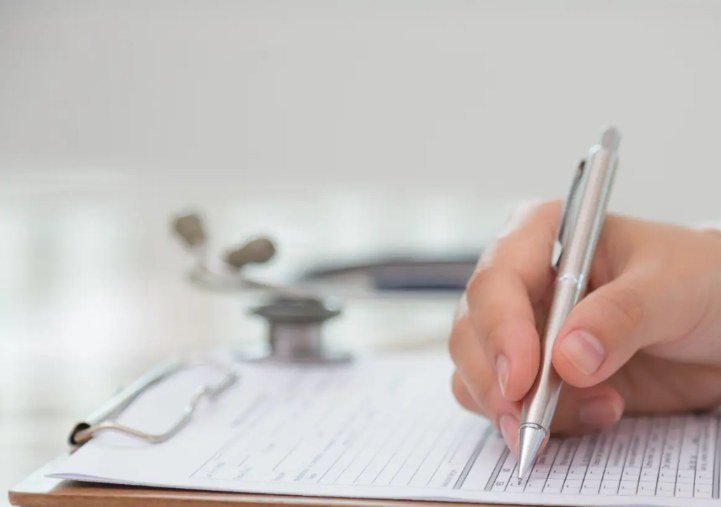 Hand som fyller i ett medicinskt intyg bredvid ett stetoskop