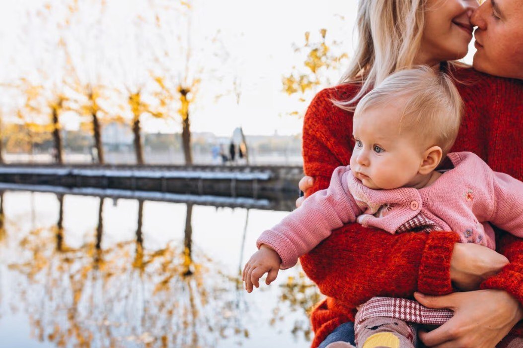 Föräldrar med en bebis i rosa tröja vid en sjö på hösten